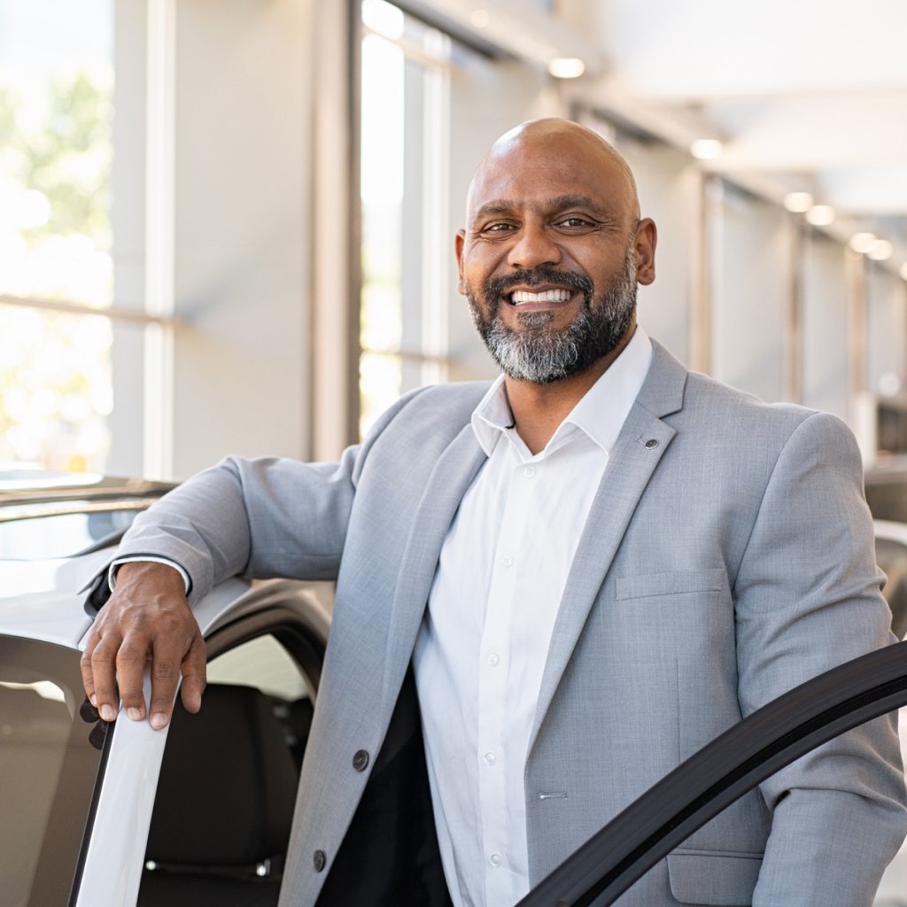 Smiling businessman with car, representing comprehensive motor fleet insurance for businesses of all sizes