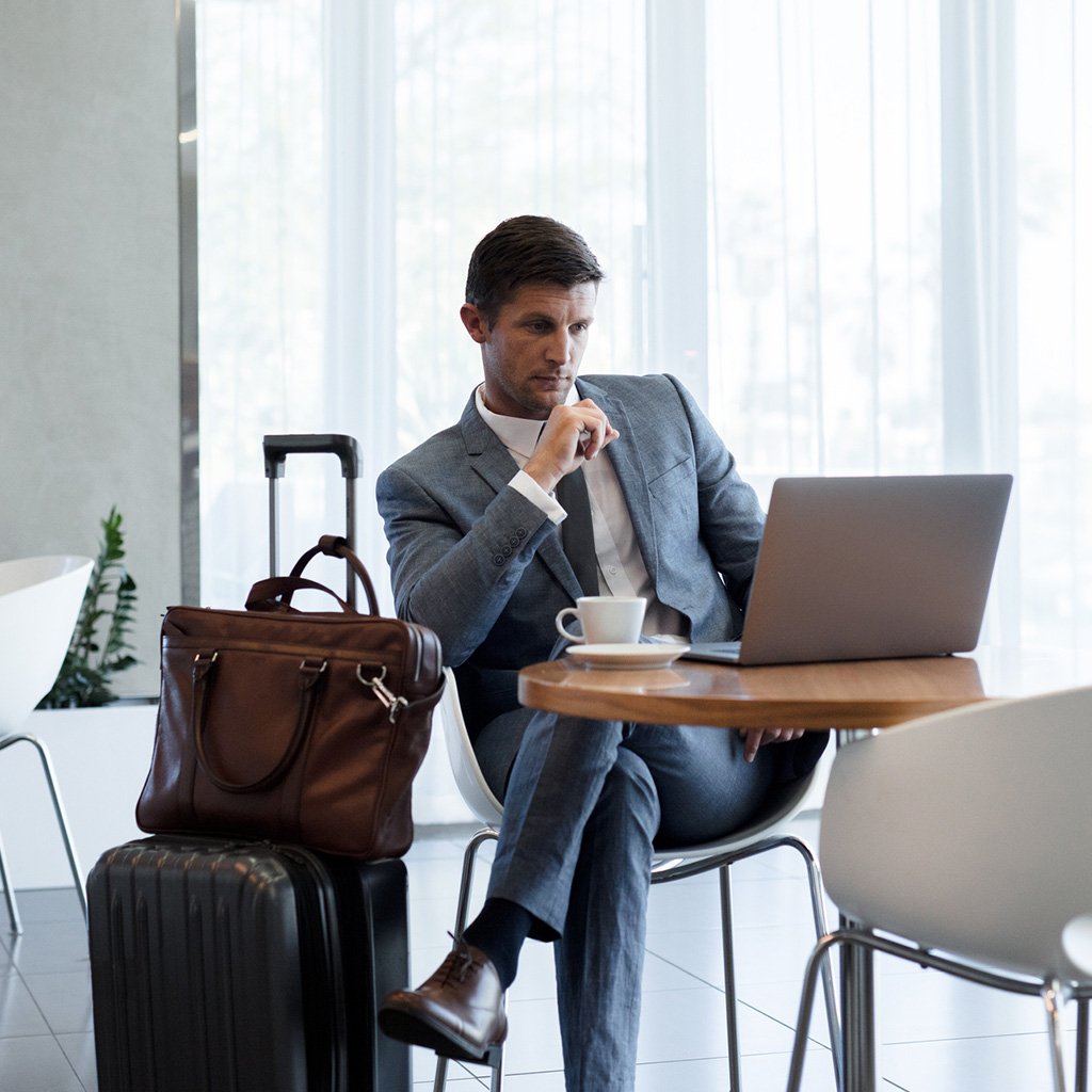Business traveler with suitcase and laptop researching UAE best online travel insurance services in an airport lounge