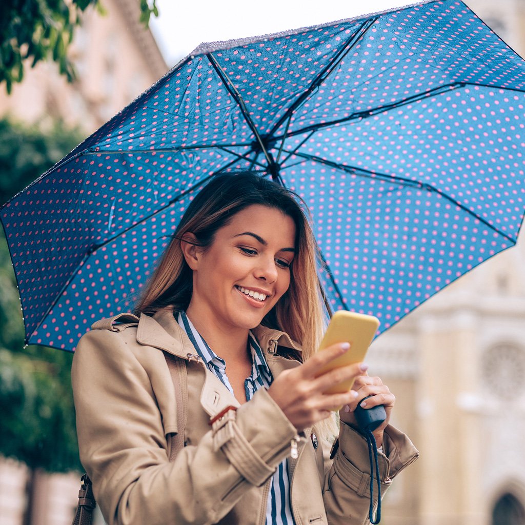 Home umbrella insurance plan in Dubai, UAE for comprehensive property coverage. Smiling woman with phone holding umbrella.